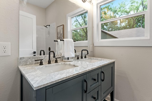 bathroom featuring a sink, tiled shower, double vanity, and a textured wall