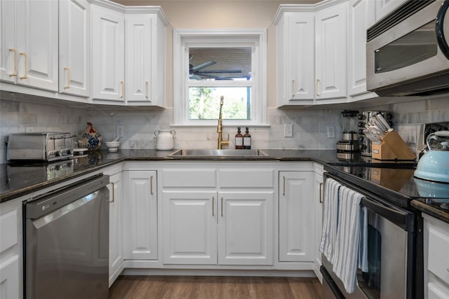 kitchen with a sink, backsplash, wood finished floors, stainless steel appliances, and white cabinets