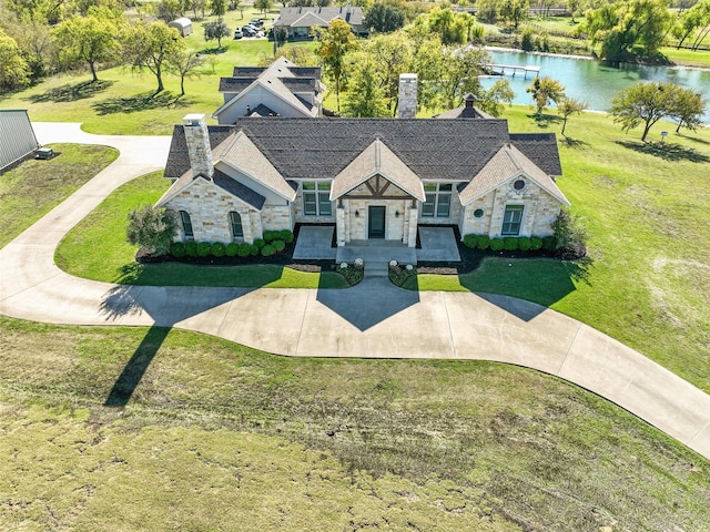 french country inspired facade with stone siding, a front lawn, a chimney, and a water view