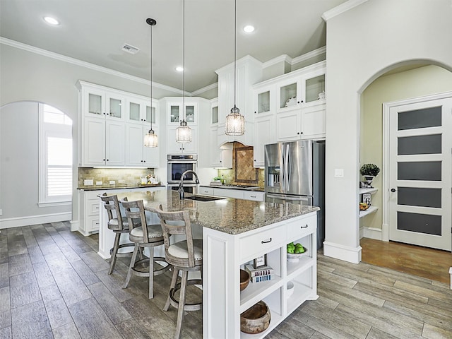 kitchen featuring backsplash, an island with sink, wood finished floors, arched walkways, and a sink