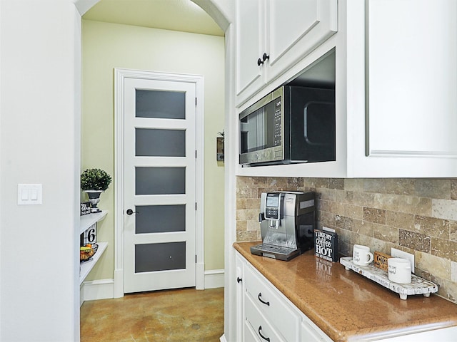 kitchen featuring stainless steel microwave, backsplash, white cabinetry, and concrete floors