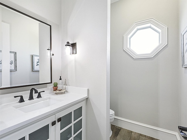 half bathroom with toilet, vanity, baseboards, and wood finished floors