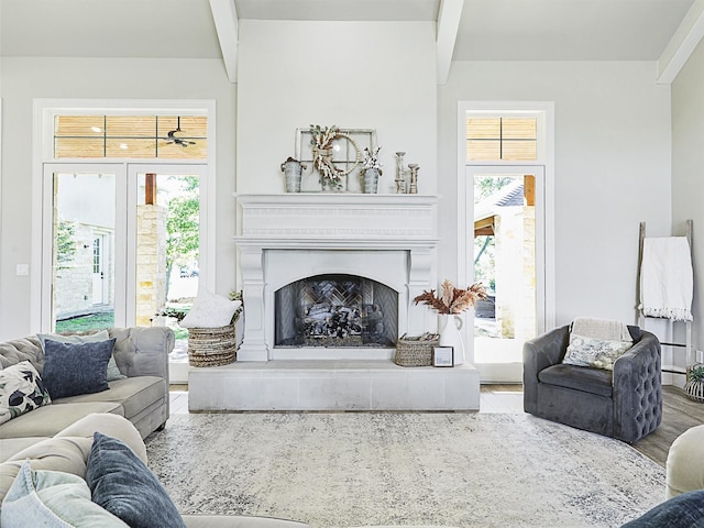 living area featuring beamed ceiling, a fireplace with raised hearth, and wood finished floors