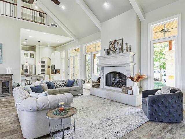 living room featuring beam ceiling, visible vents, a fireplace with raised hearth, and wood finished floors