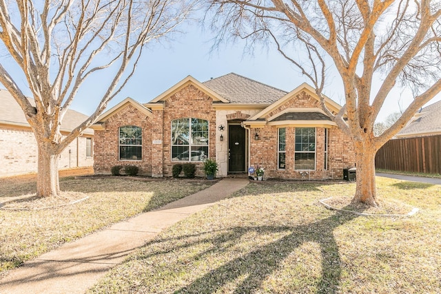 single story home with a front lawn, fence, brick siding, and a shingled roof