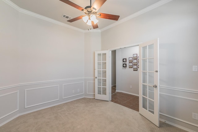 carpeted spare room with visible vents, crown molding, french doors, a decorative wall, and a ceiling fan