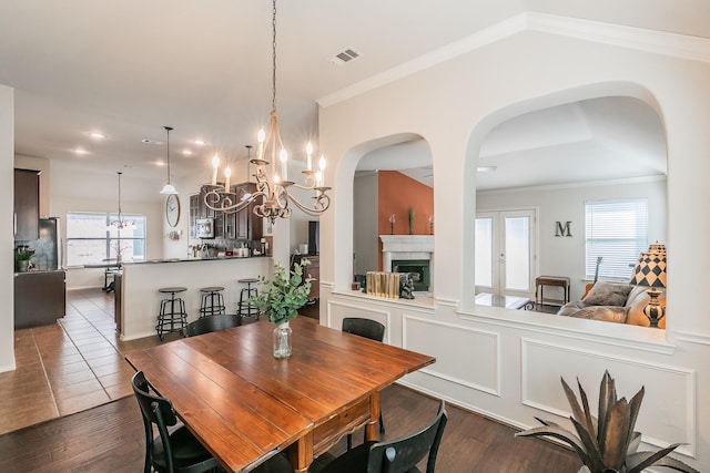 dining area featuring visible vents, ornamental molding, dark wood-style floors, a fireplace, and a chandelier