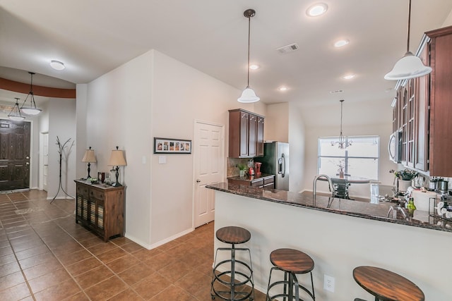 kitchen featuring visible vents, dark stone countertops, a peninsula, a kitchen breakfast bar, and stainless steel appliances