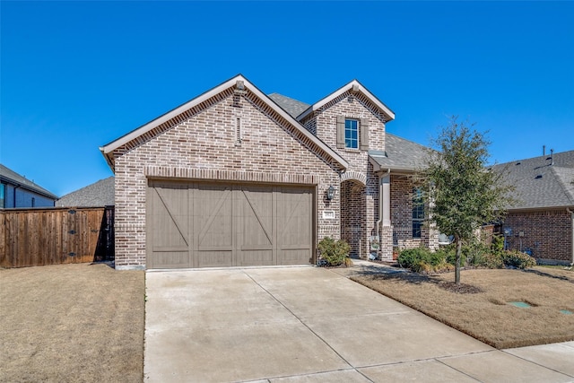 french country style house featuring driveway, fence, roof with shingles, a garage, and brick siding