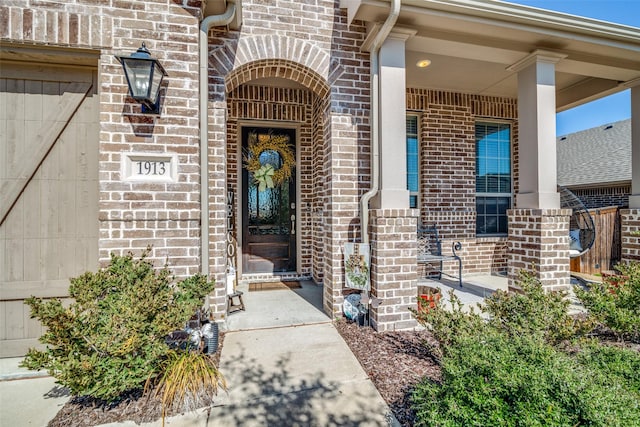 view of exterior entry with brick siding and a porch