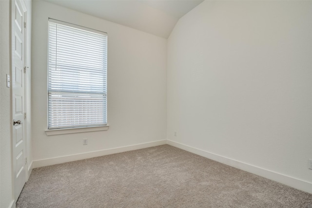 carpeted spare room featuring lofted ceiling and baseboards