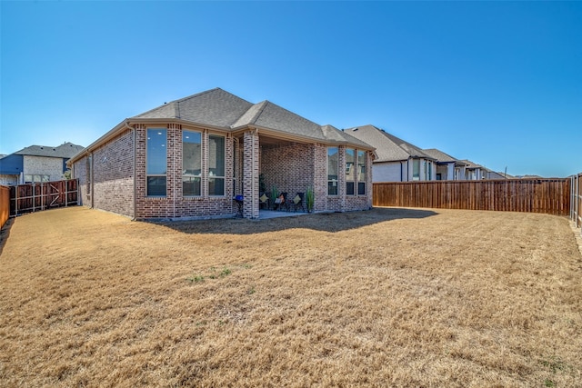 back of house with a yard, brick siding, and a fenced backyard