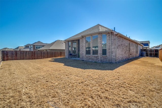 back of property featuring brick siding, a lawn, and a fenced backyard