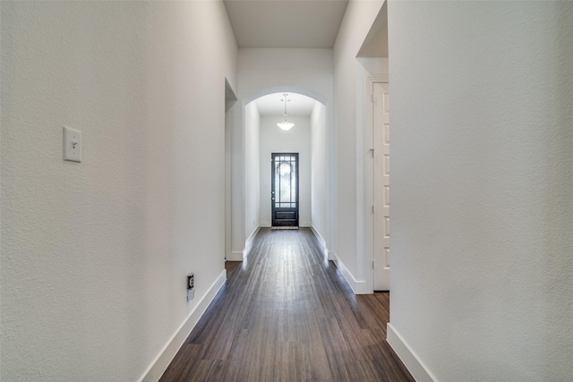 hallway featuring dark wood finished floors, baseboards, and arched walkways