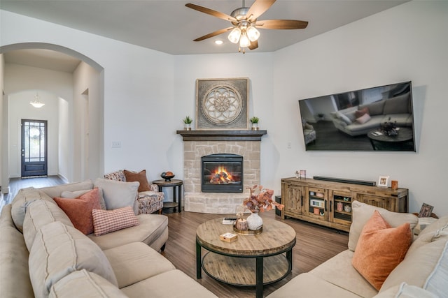 living area with a ceiling fan, wood finished floors, recessed lighting, arched walkways, and a stone fireplace