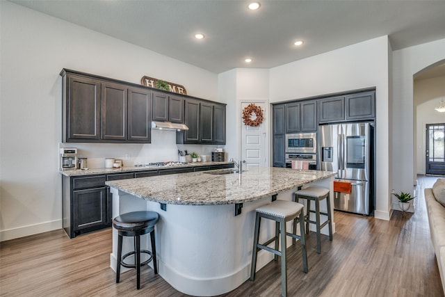 kitchen with arched walkways, a sink, stainless steel appliances, under cabinet range hood, and a kitchen bar