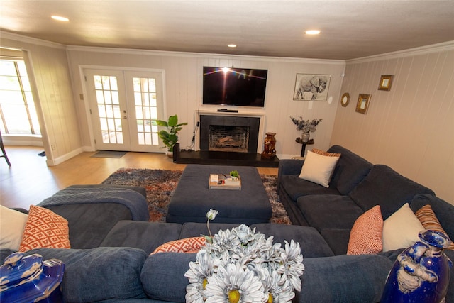 living room with a fireplace with raised hearth, ornamental molding, recessed lighting, french doors, and wood finished floors