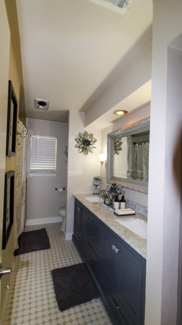 bathroom with a sink, baseboards, toilet, and double vanity