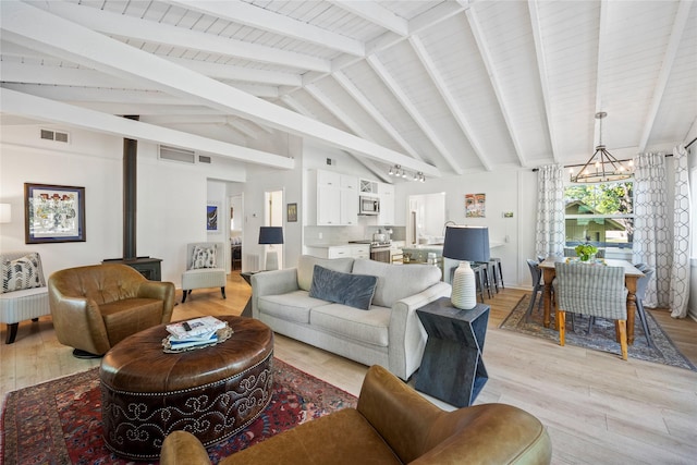 living room with visible vents, lofted ceiling with beams, a wood stove, light wood-style floors, and a chandelier