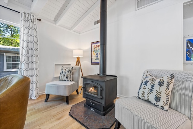 sitting room with visible vents, vaulted ceiling with beams, wood finished floors, and a wood stove