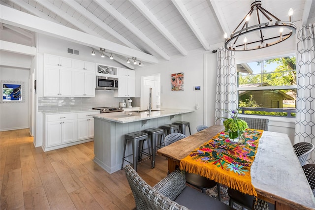 kitchen featuring visible vents, lofted ceiling with beams, a sink, appliances with stainless steel finishes, and tasteful backsplash