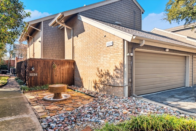 view of side of property with driveway, brick siding, an attached garage, and fence