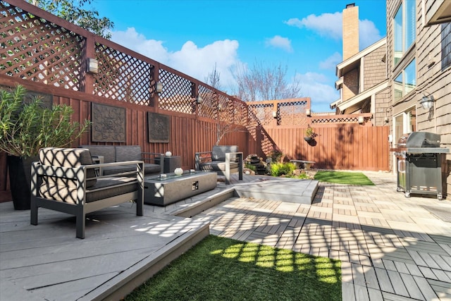 view of patio with grilling area, a wooden deck, an outdoor living space with a fire pit, and a fenced backyard