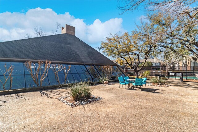 exterior space featuring a shingled roof, a patio, fence, and a chimney