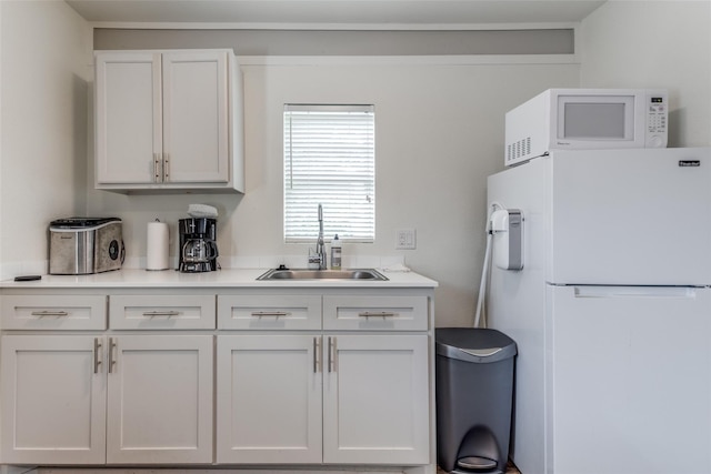 kitchen with a sink, white appliances, white cabinets, and light countertops