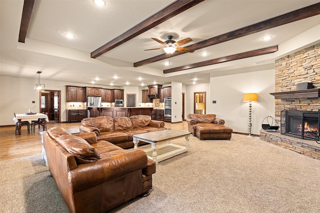 living room featuring baseboards, beam ceiling, a stone fireplace, and a ceiling fan