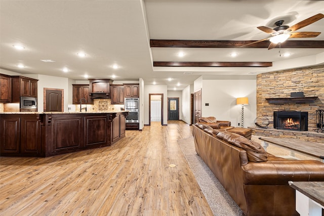 living room with light wood finished floors, beam ceiling, recessed lighting, a fireplace, and a ceiling fan