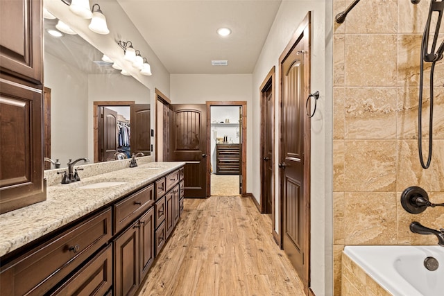 bathroom featuring a sink, tiled shower / bath, wood finished floors, and double vanity