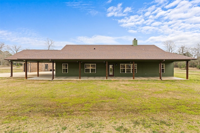 rear view of house featuring a shingled roof, a patio, a yard, and a chimney