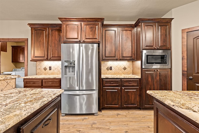 kitchen featuring washer and clothes dryer, backsplash, appliances with stainless steel finishes, light wood finished floors, and light stone countertops