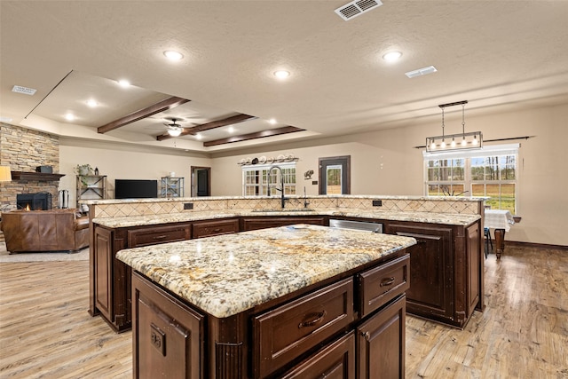 kitchen with visible vents, a kitchen island, light wood-style flooring, a sink, and a stone fireplace