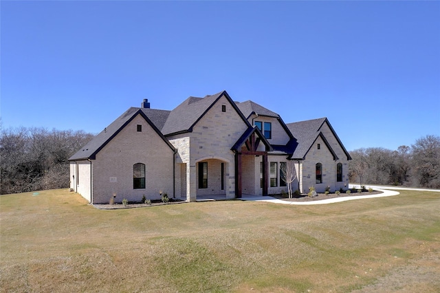 french provincial home featuring stone siding, brick siding, a chimney, and a front yard