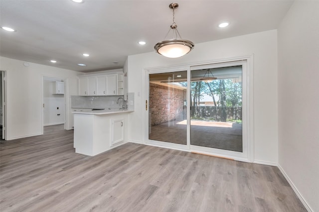 kitchen with light wood-type flooring, tasteful backsplash, white cabinetry, a peninsula, and light countertops