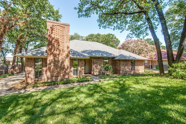 view of front of home featuring a front lawn, fence, a shingled roof, brick siding, and a chimney