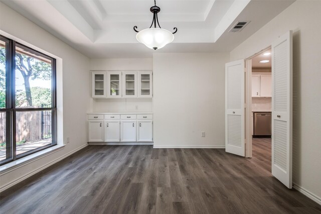 unfurnished dining area with visible vents, a raised ceiling, baseboards, and dark wood finished floors