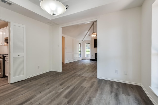 spare room featuring visible vents, vaulted ceiling, a fireplace, dark wood-style floors, and a ceiling fan