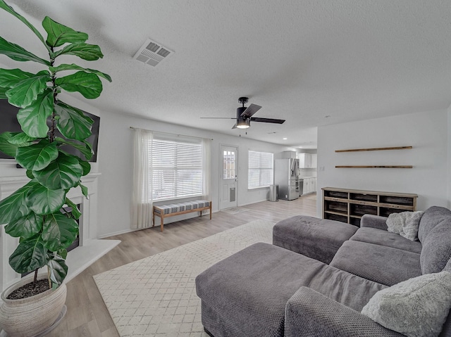 living area with visible vents, a ceiling fan, a textured ceiling, a fireplace, and light wood finished floors