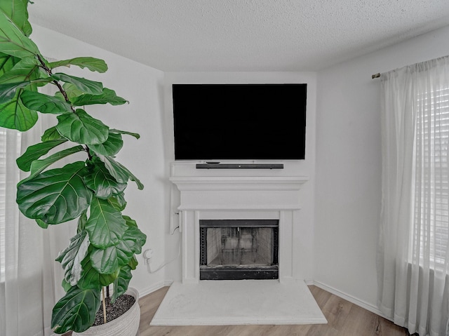 unfurnished living room featuring a fireplace with raised hearth, a textured ceiling, baseboards, and wood finished floors