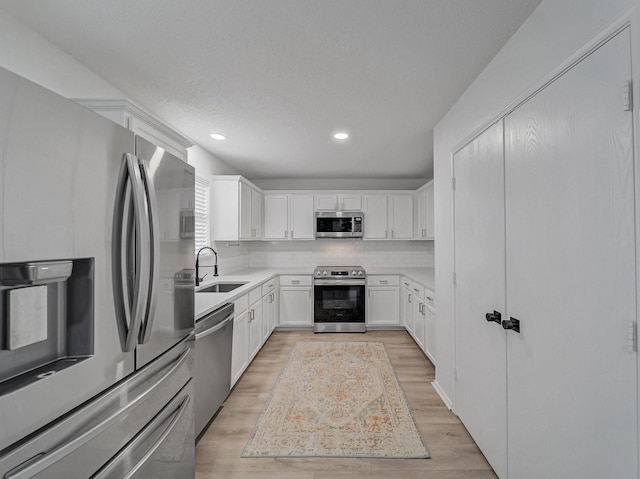 kitchen with a sink, backsplash, white cabinetry, appliances with stainless steel finishes, and light wood finished floors