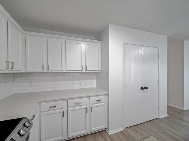 kitchen featuring light wood finished floors, light countertops, decorative backsplash, white cabinets, and stainless steel range