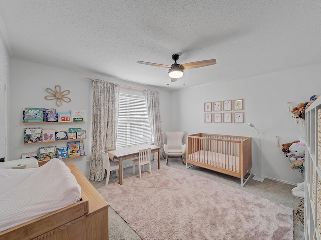 carpeted bedroom with a nursery area, a textured ceiling, and ceiling fan