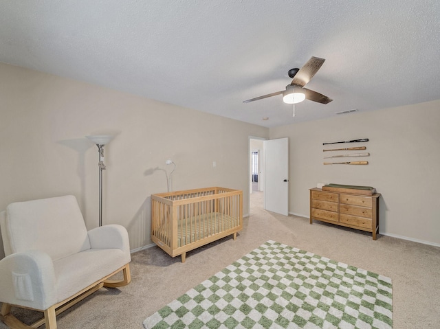 carpeted bedroom with a ceiling fan, baseboards, visible vents, a crib, and a textured ceiling