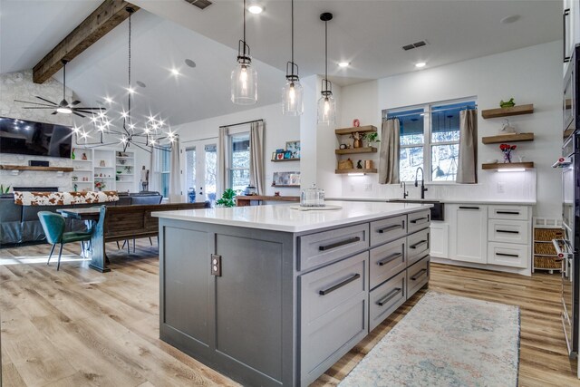 kitchen featuring visible vents, open shelves, lofted ceiling with beams, light countertops, and a sink