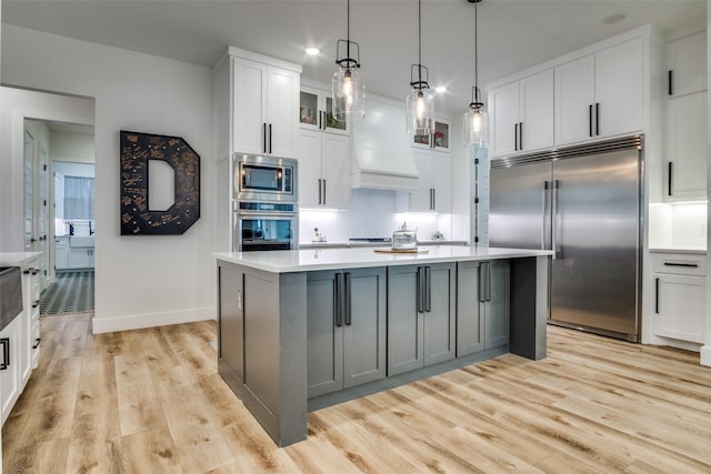 kitchen with custom exhaust hood, light wood-style flooring, light countertops, built in appliances, and white cabinetry