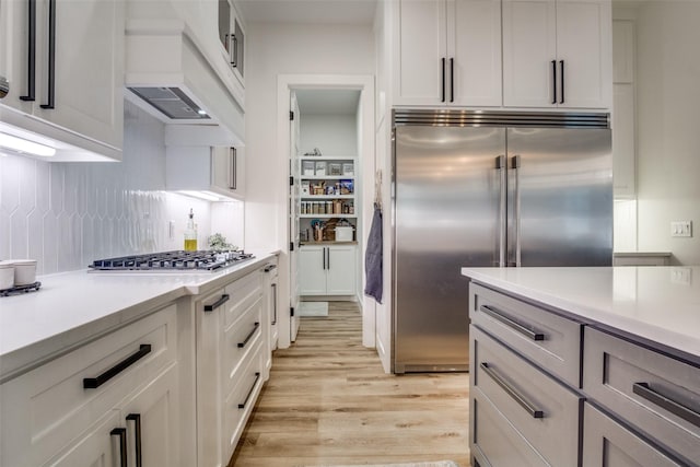 kitchen featuring light countertops, white cabinets, appliances with stainless steel finishes, light wood-type flooring, and backsplash