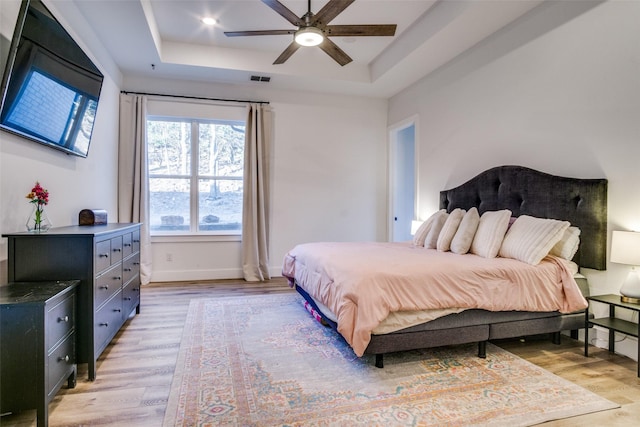 bedroom with a tray ceiling, baseboards, visible vents, and light wood-style flooring